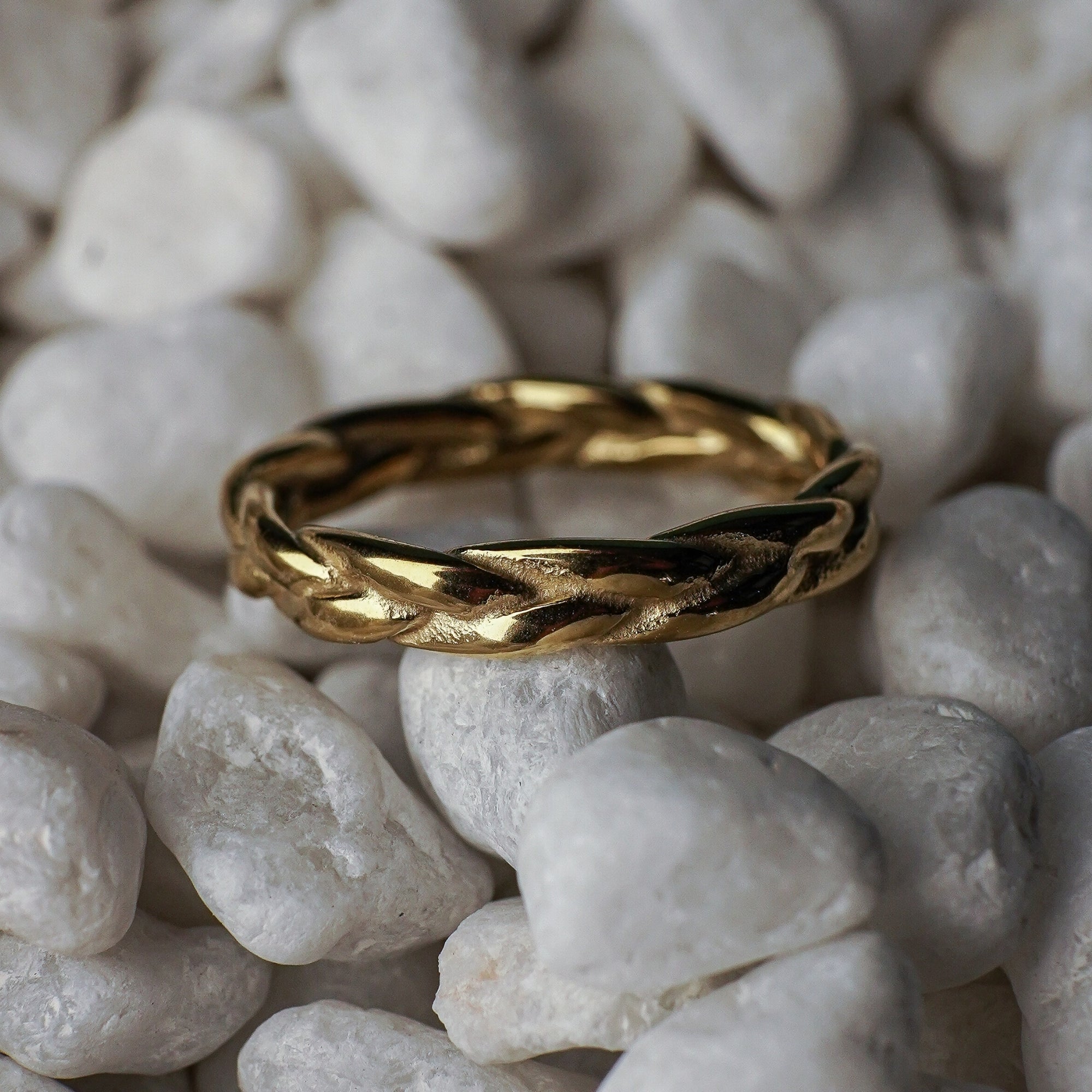 Gold ring with braided design on white pebbles