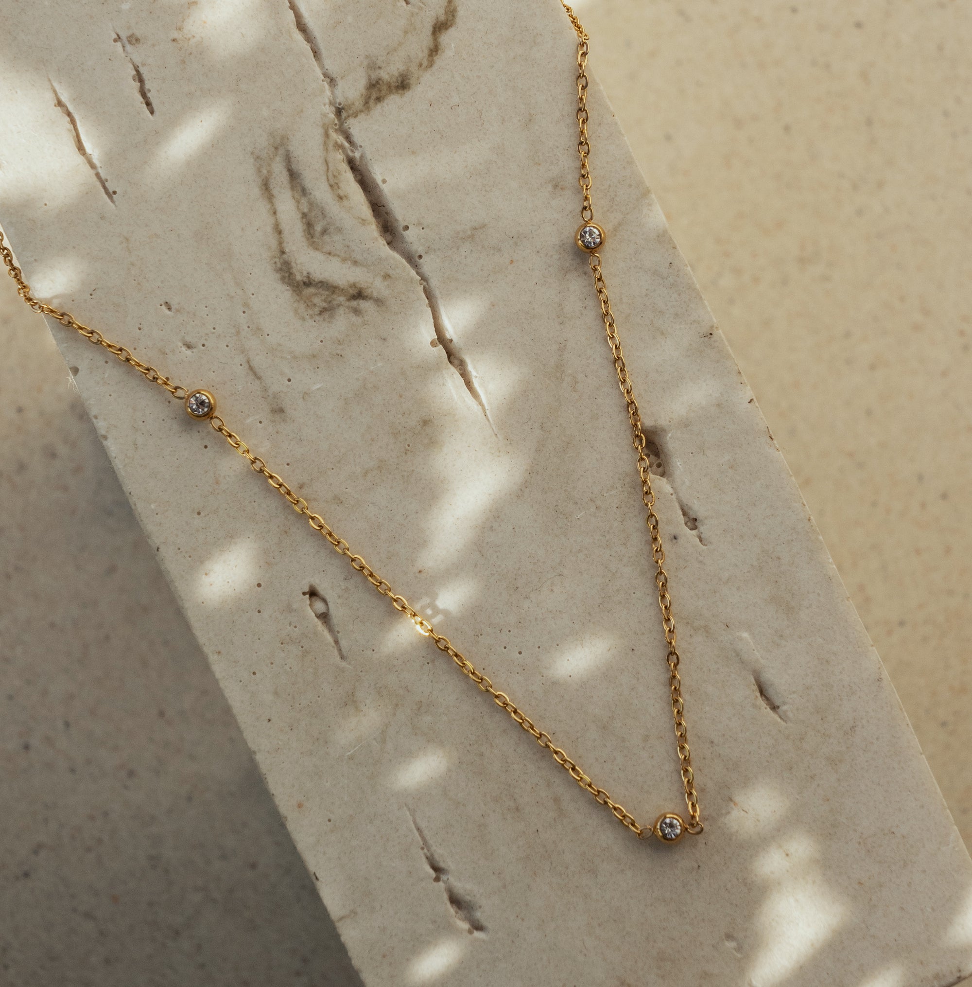 A delicate gold chain necklace with small sparkling zirconia stones laid out on a flat surface.