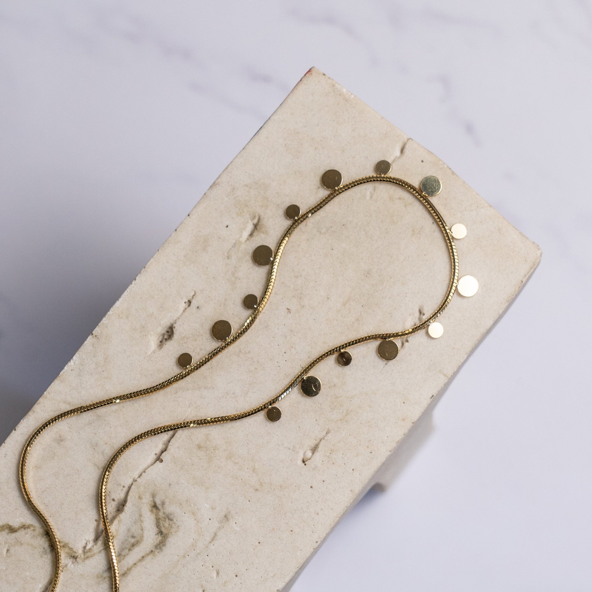 A gold-colored necklace with a unique and trendy design, displayed on a beige background.
