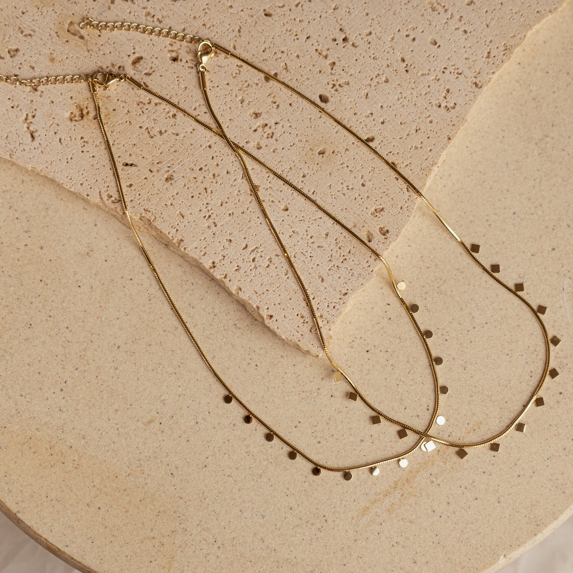 A gold-colored necklace with small, regular intervals of pearls displayed on a beige stone surface.
