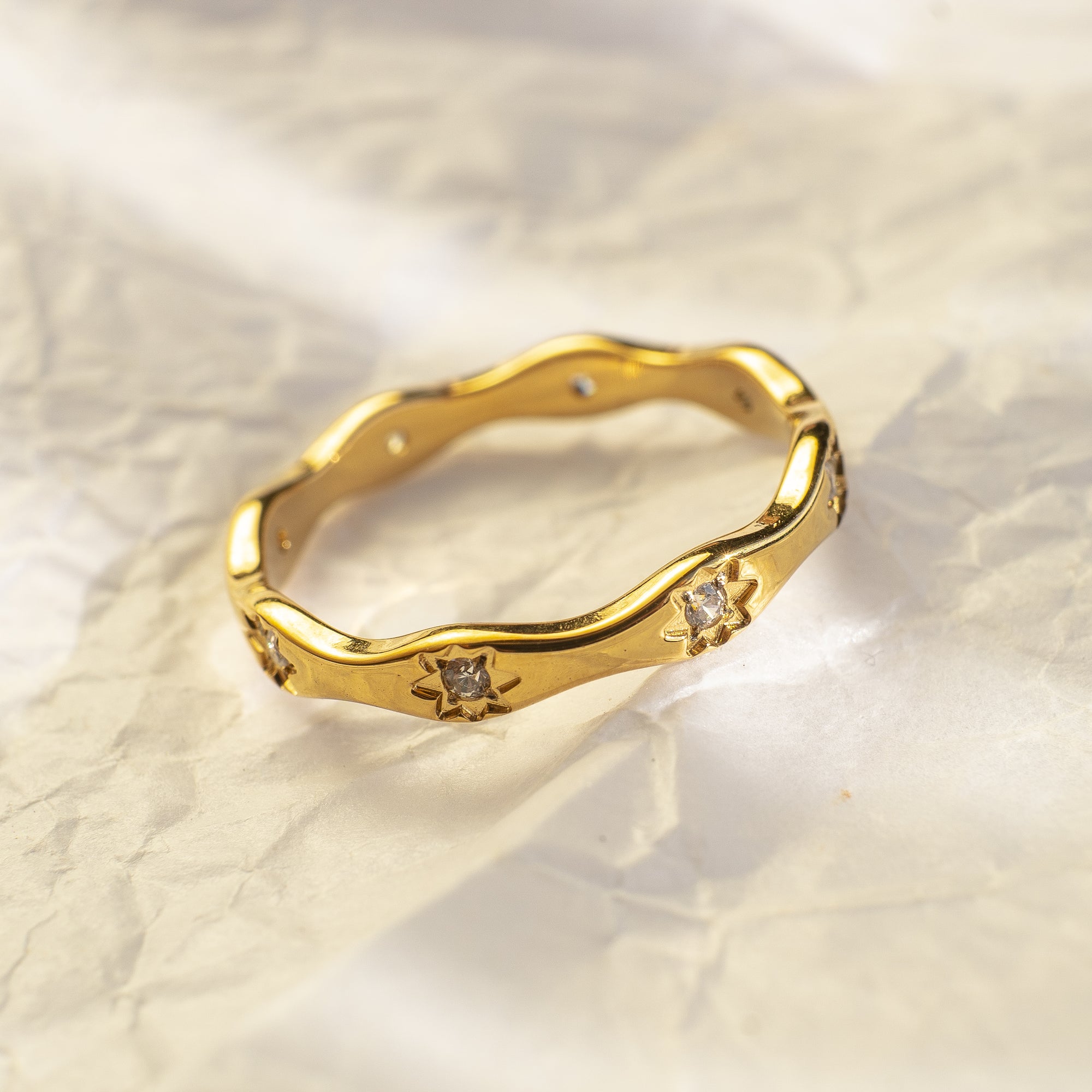 Gold ring with diamond accents on a textured beige background