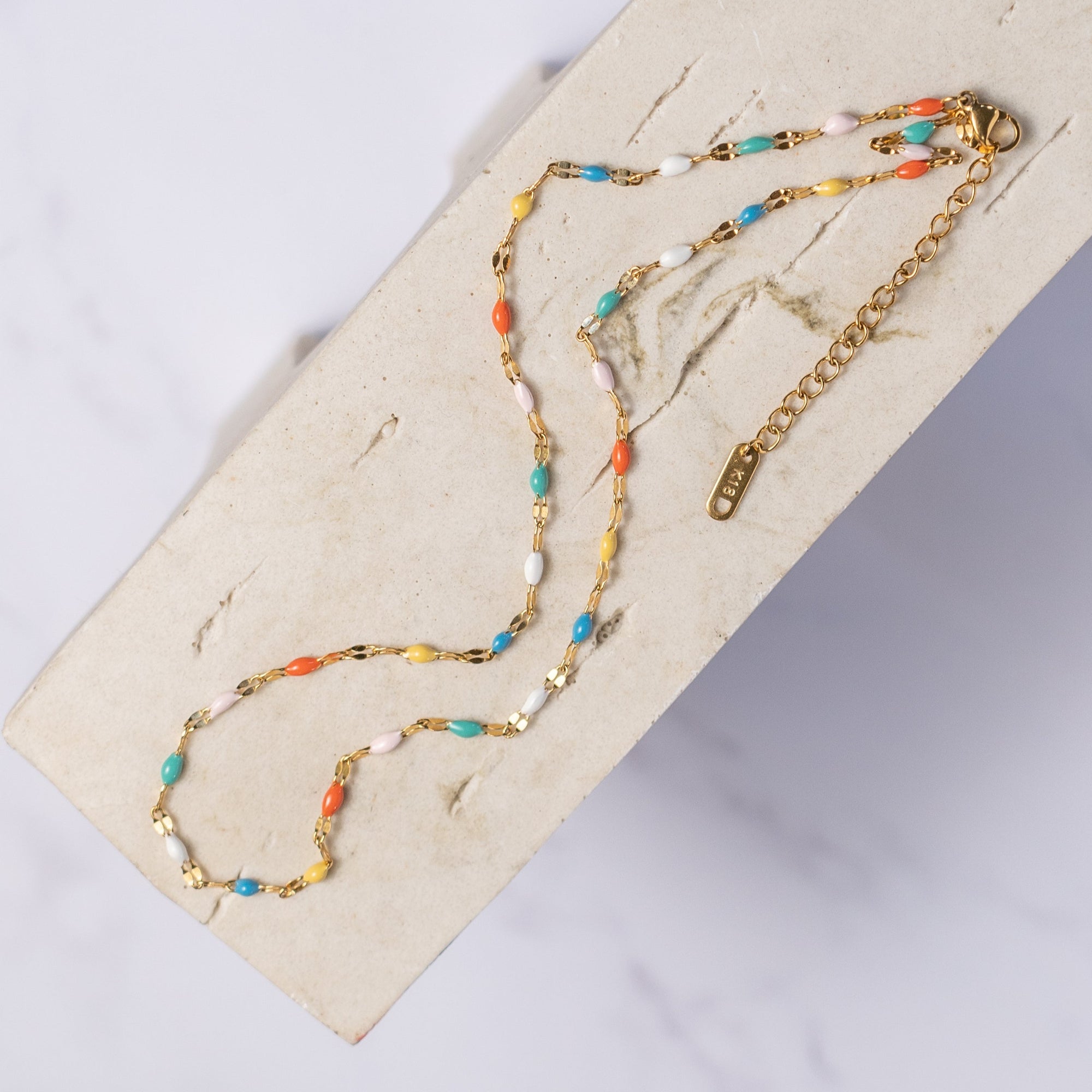 A colorful beaded choker necklace displayed on a wooden surface, with a combination of metallic and matte beads in a rainbow pattern.