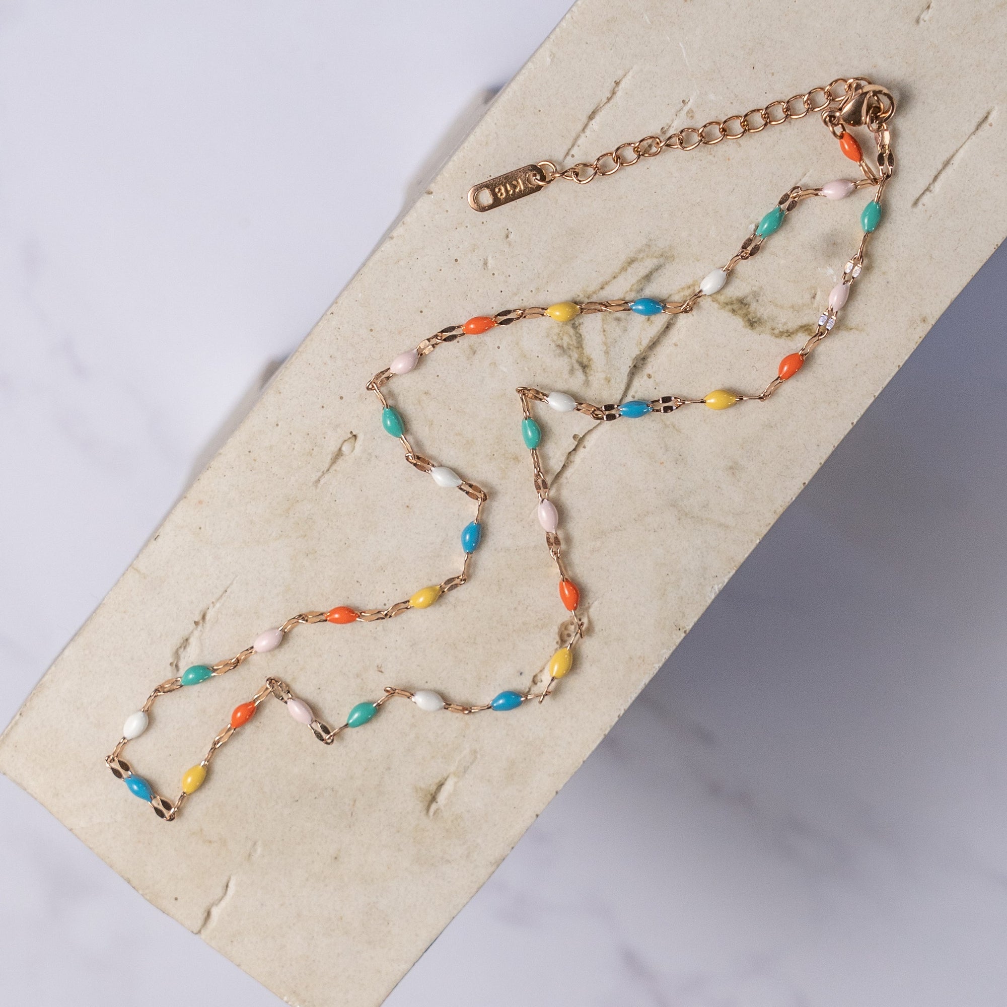 A colorful beaded choker necklace displayed on a wooden surface, with a combination of metallic and matte beads in a rainbow pattern.