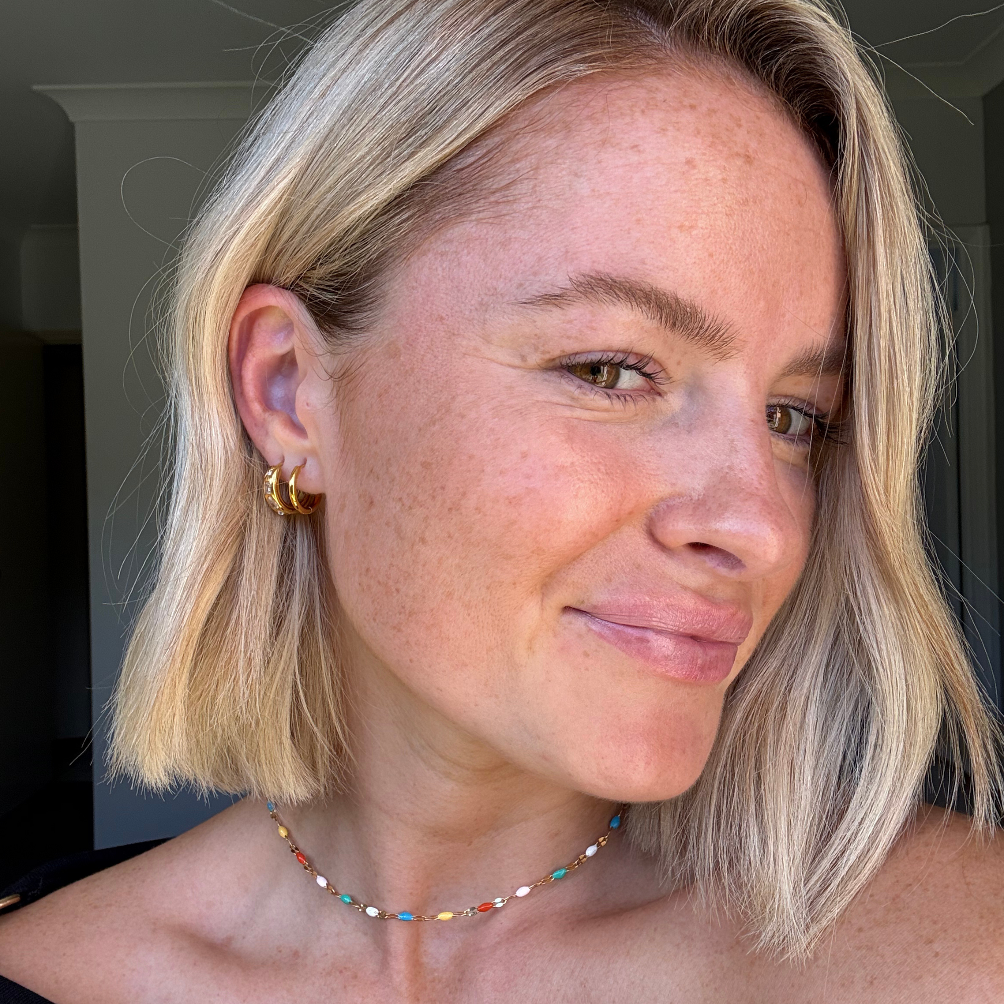 A beautiful woman wearing two gold hoop earrings and a colorful necklace