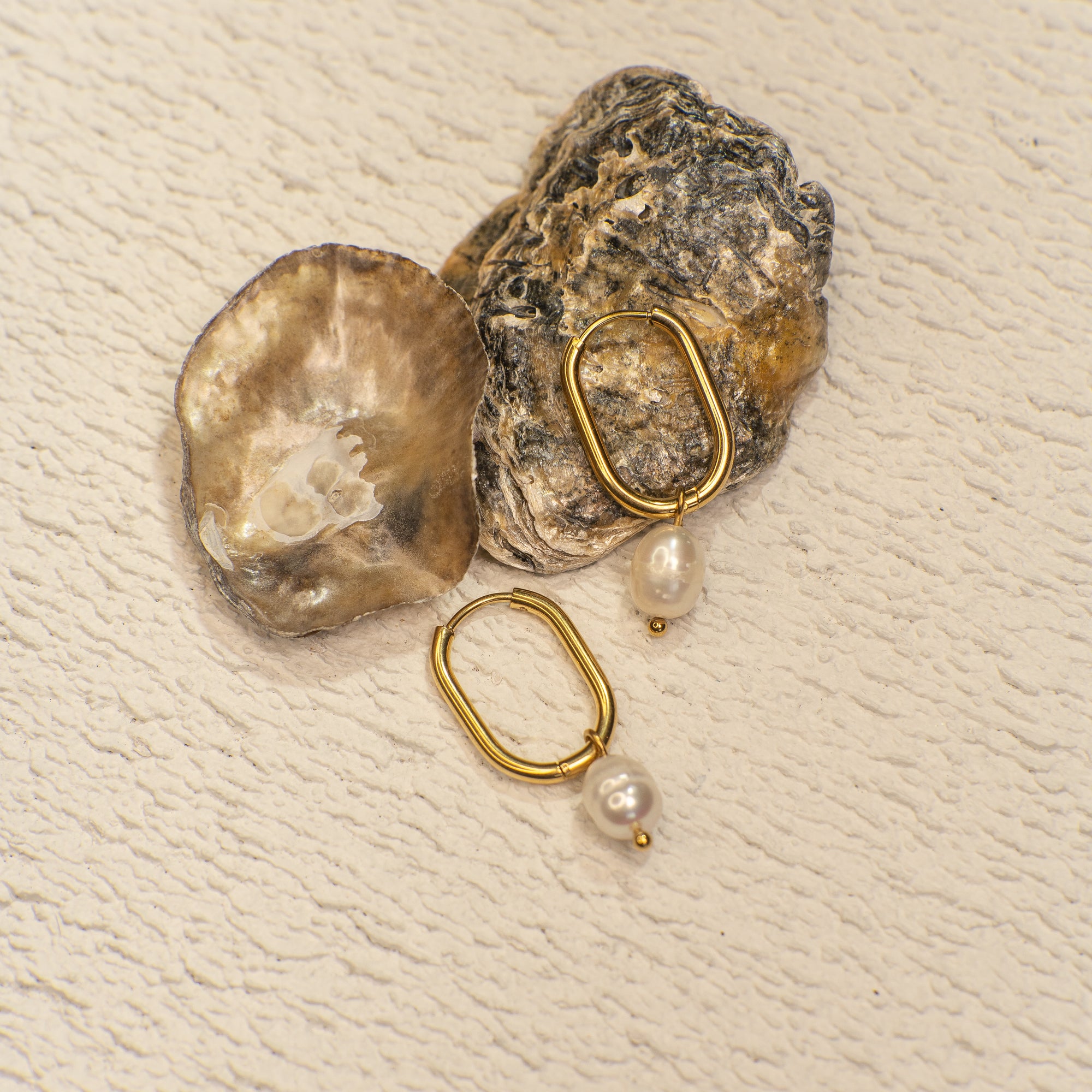 Gold hoop earrings with pearls on a textured beige surface