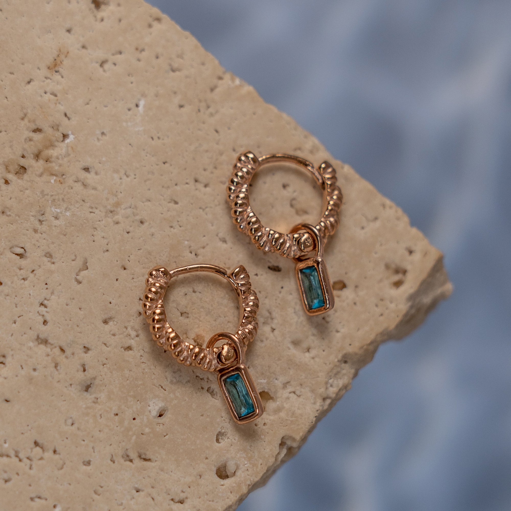 A pair of rose gold earrings with Aquamarine drop pendant on a textured surface