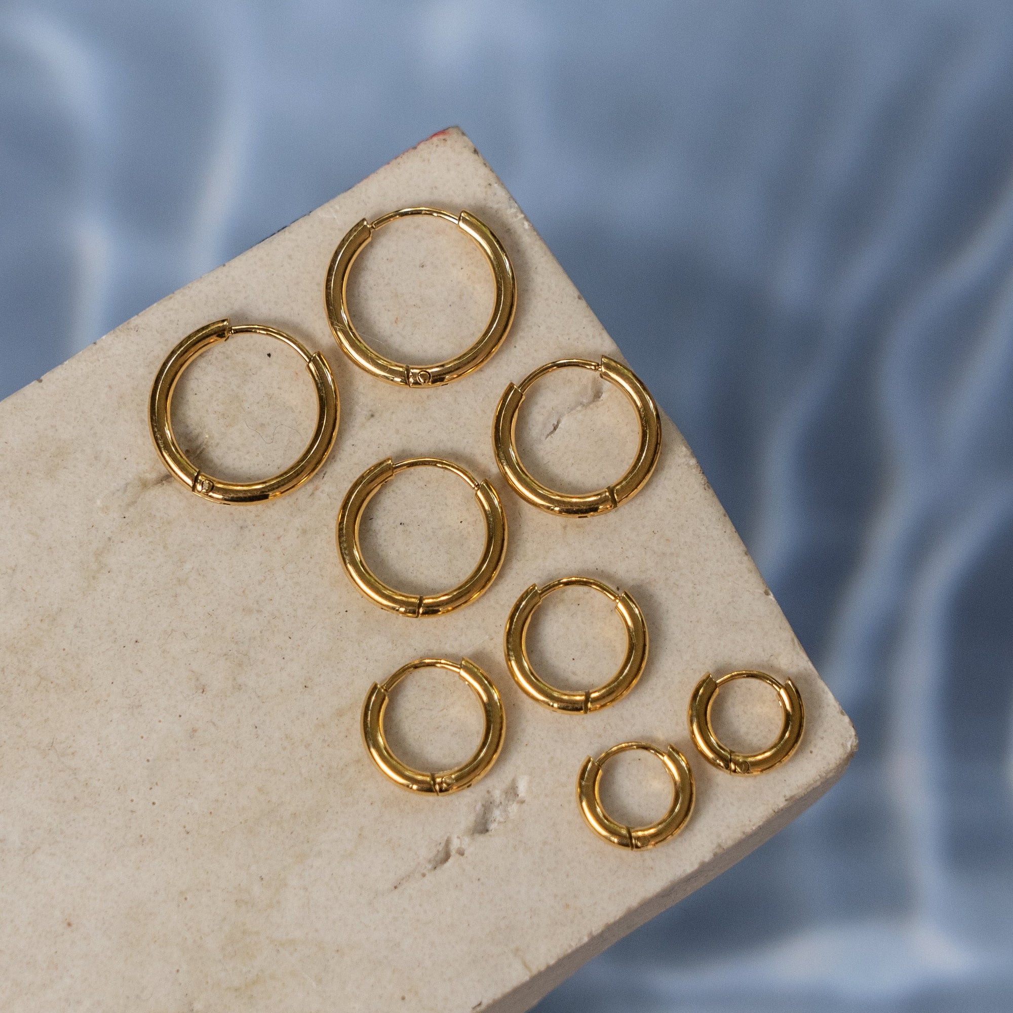 A collection of gold hoop earrings of various sizes displayed on a flat surface with a textured background.