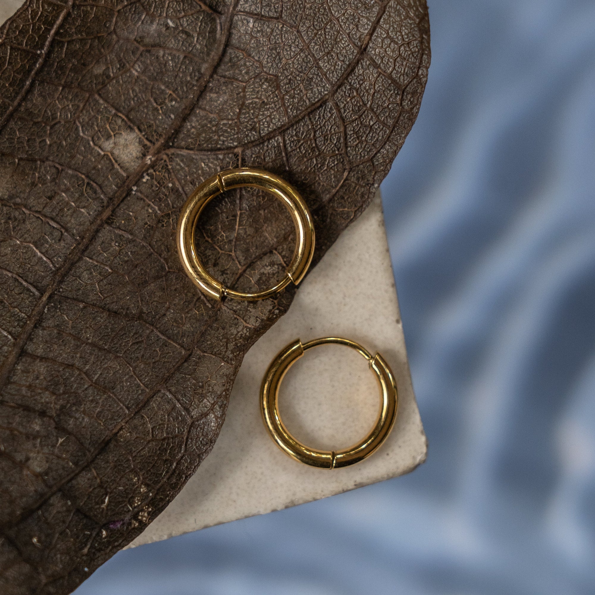 A collection of gold hoop earrings of various sizes displayed on a flat surface with a textured background.