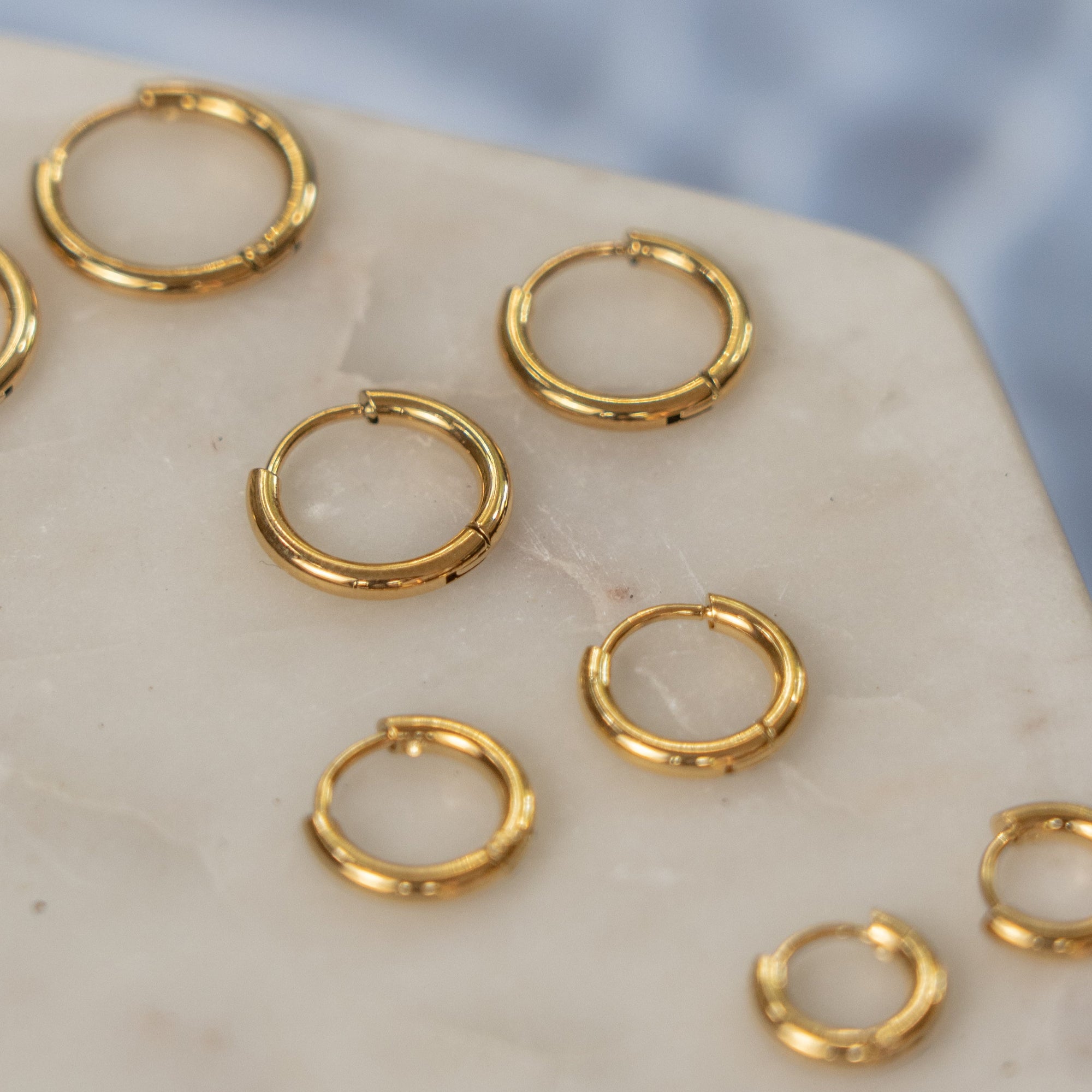 A collection of gold hoop earrings on a beige surface