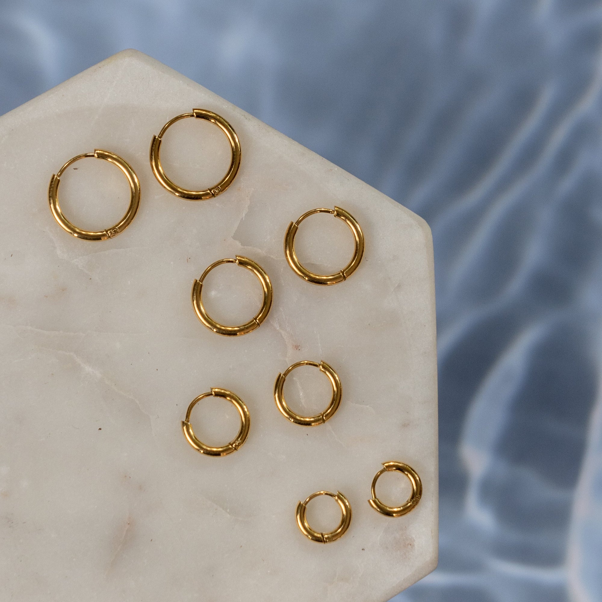 A collection of gold earrings with different sizes on a beige stuface