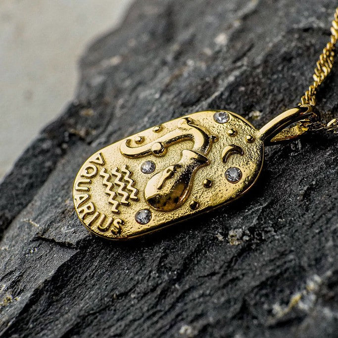 Gold Aquarius Zodiac Sign pendant on a dark stone surface