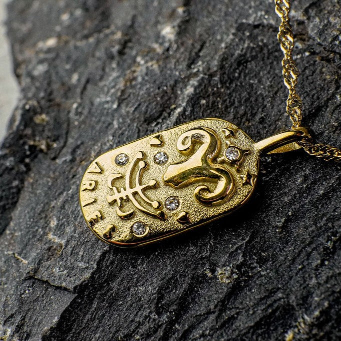 Gold pendant with Aries Zodiac Sign Design on a dark stone surface