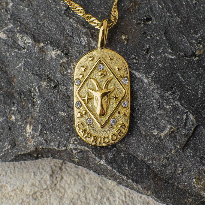 Gold Capricorn Zodiac Sign pendant necklace on a stone background