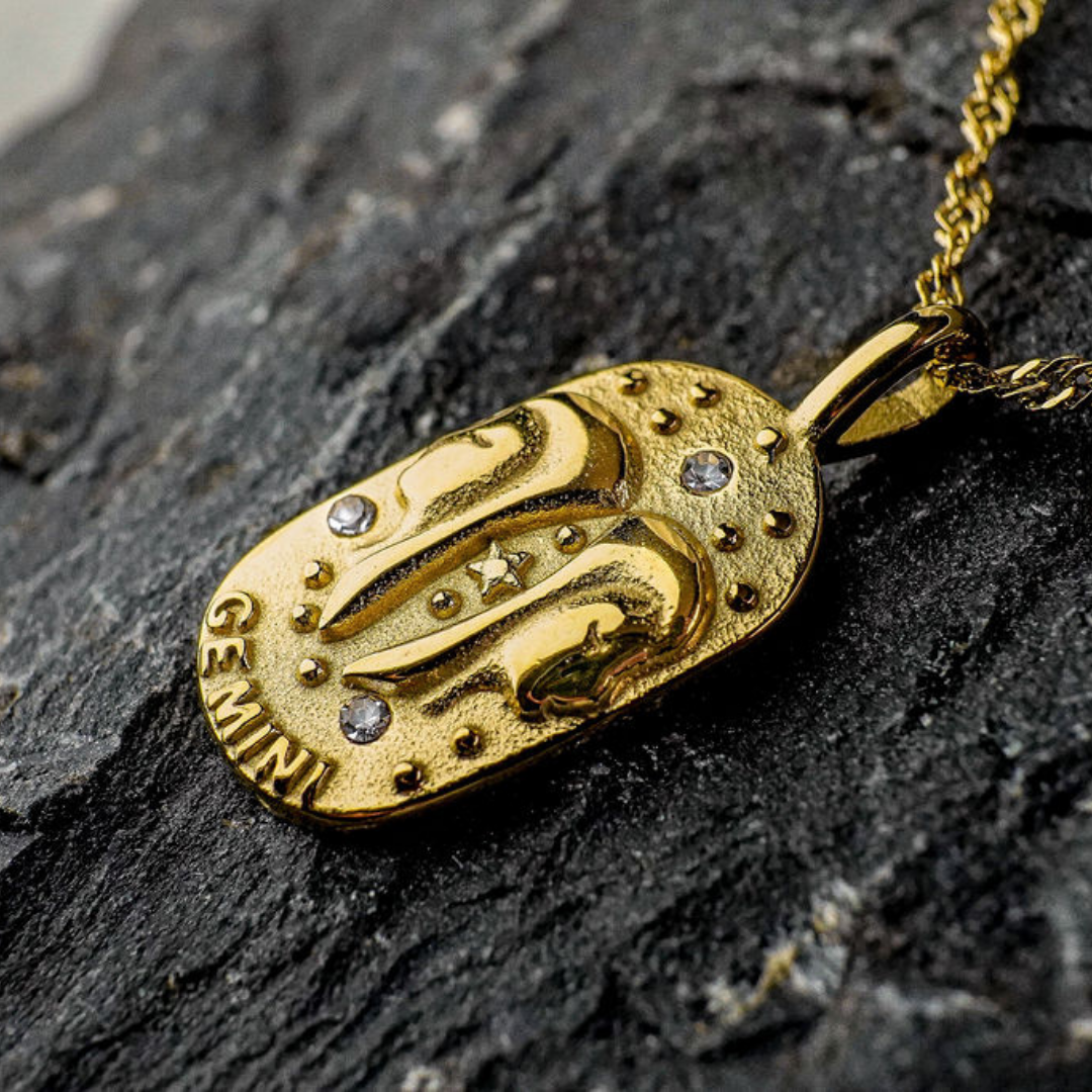 Gold pendant with Gemini Zodiac engraving on a dark stone surface