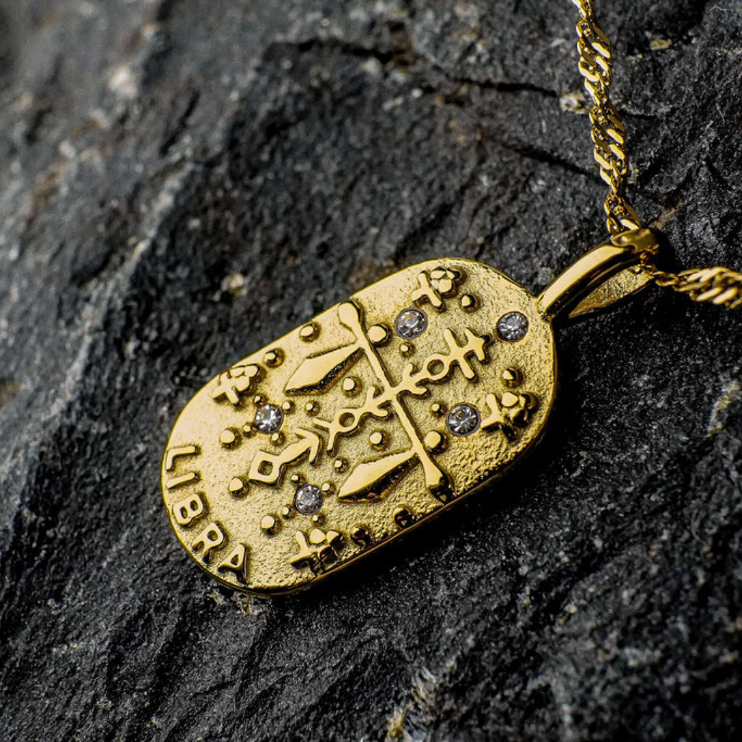 Gold pendant with Libra Zodiac Sign design on a dark stone surface