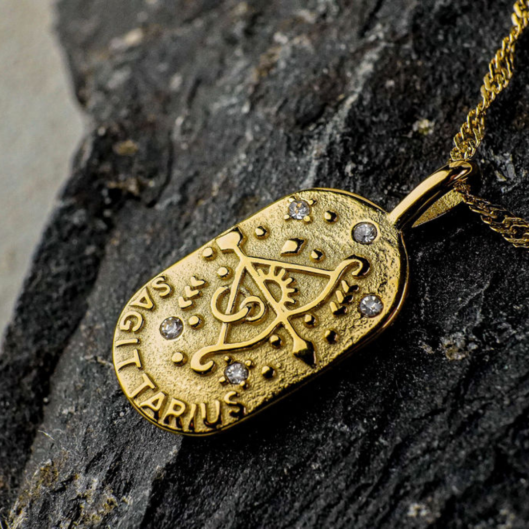 Gold pendant with Sagittarius Zodiac Sign design on a dark stone surface