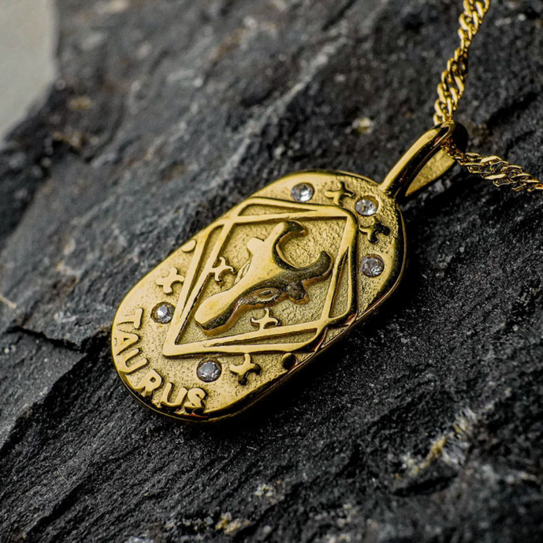 Gold Taurus Zodiac pendant with diamonds on a dark stone surface
