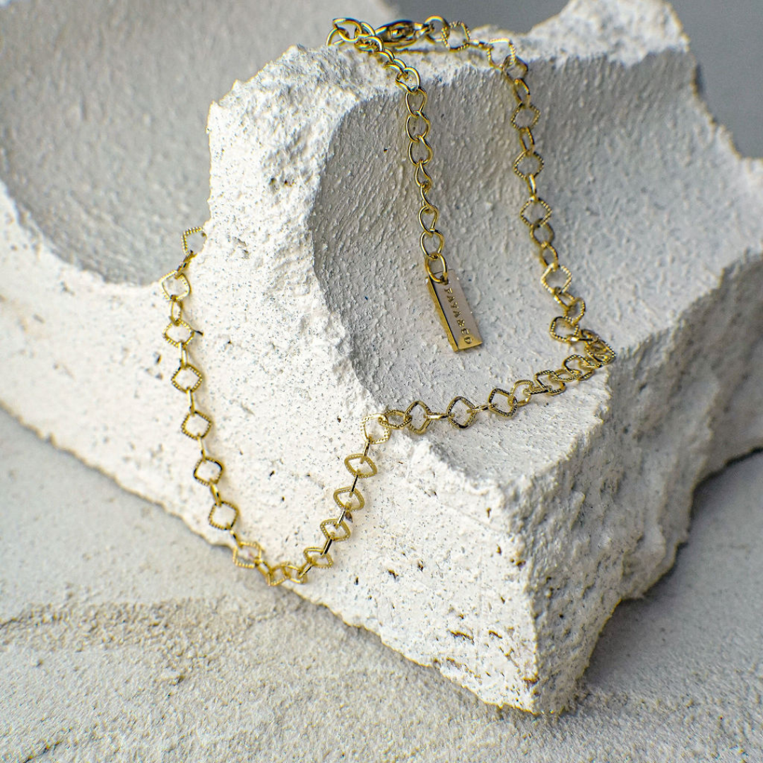 Gold chain necklace with a tag on a textured stone surface