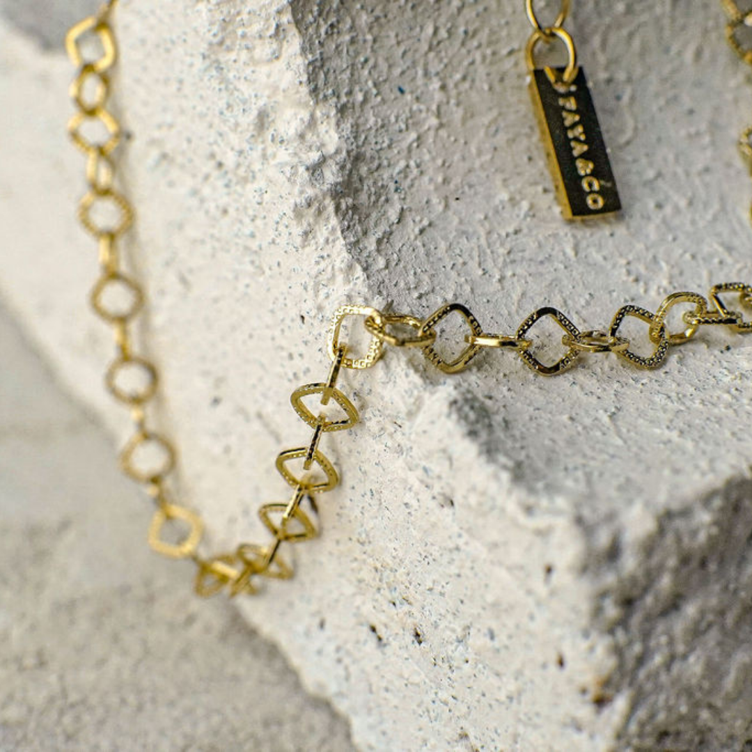 Gold chain necklace with a tag on a textured stone surface