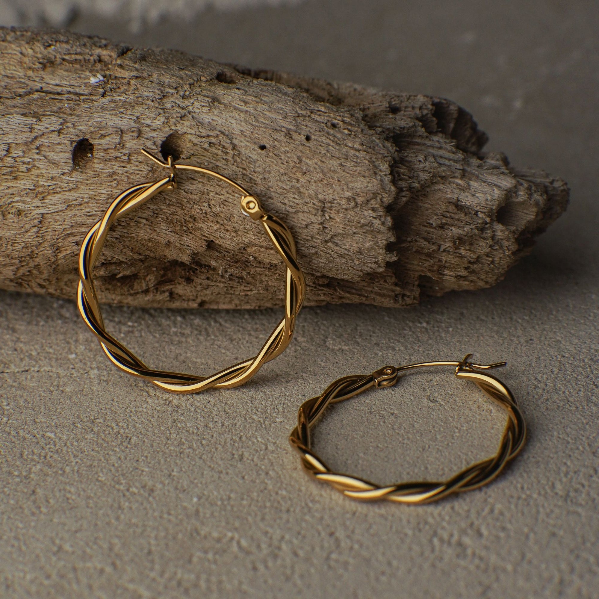 Gold hoop earrings on a textured surface with a piece of wood in the background