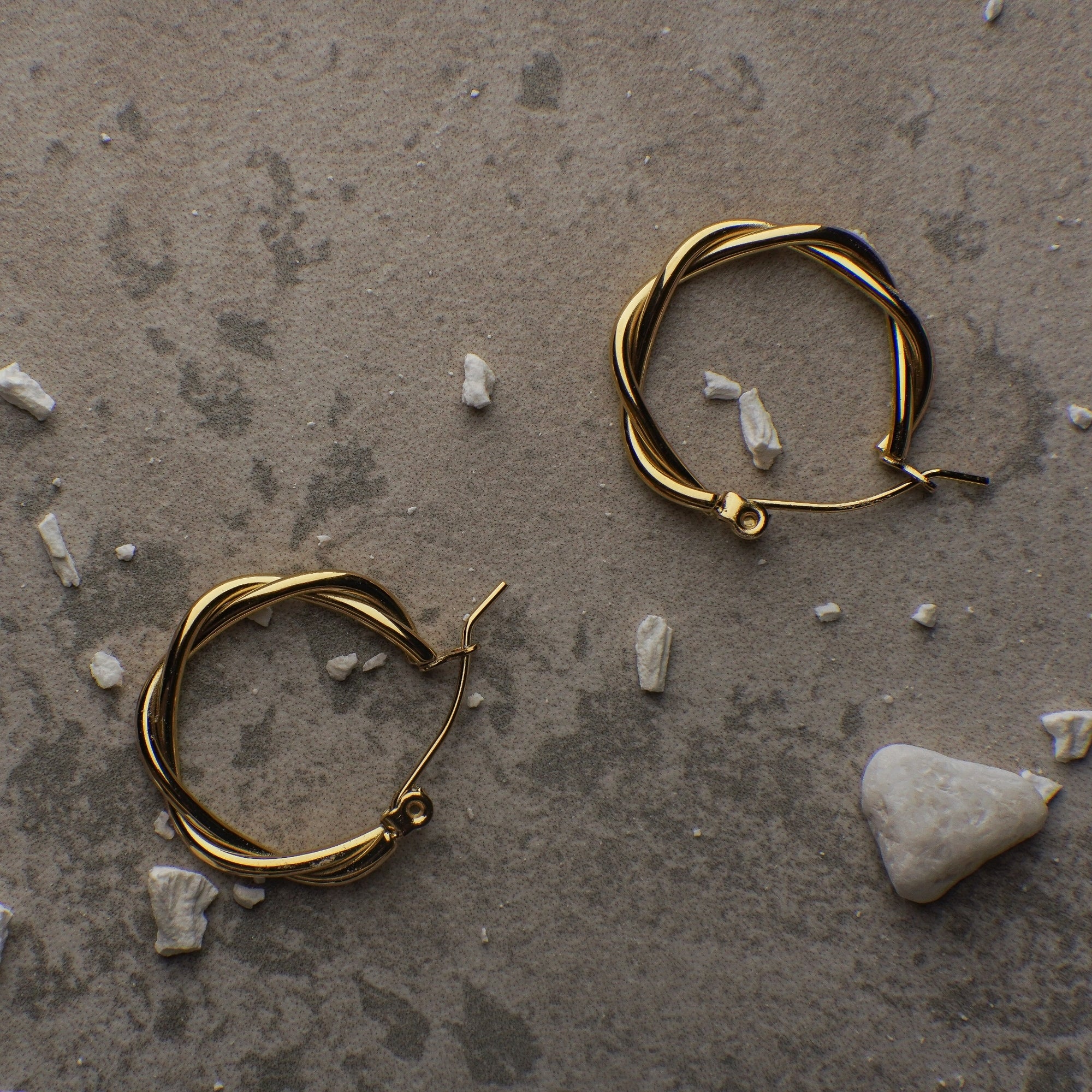 Gold hoop earrings on a textured stone surface with small stones around.