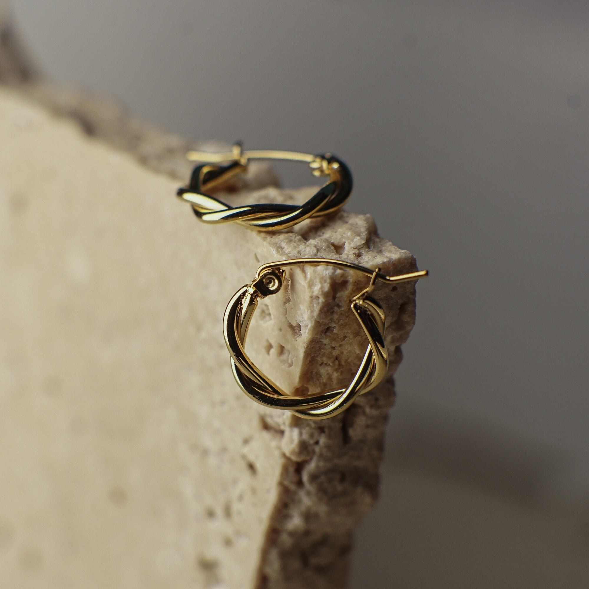 Gold hoop earrings on a textured stone surface with a neutral background
