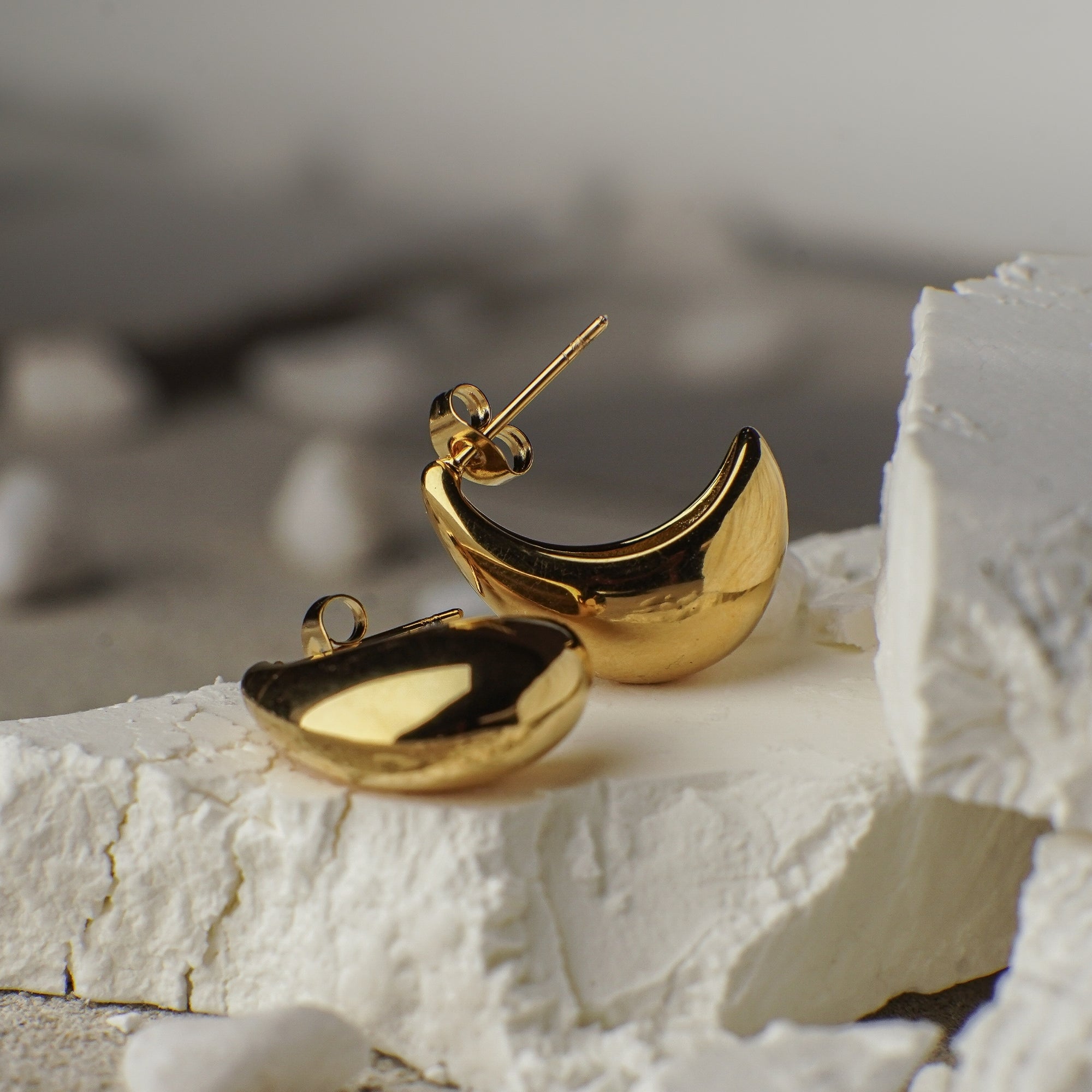 Gold hoop earrings on a textured white surface with a blurred background