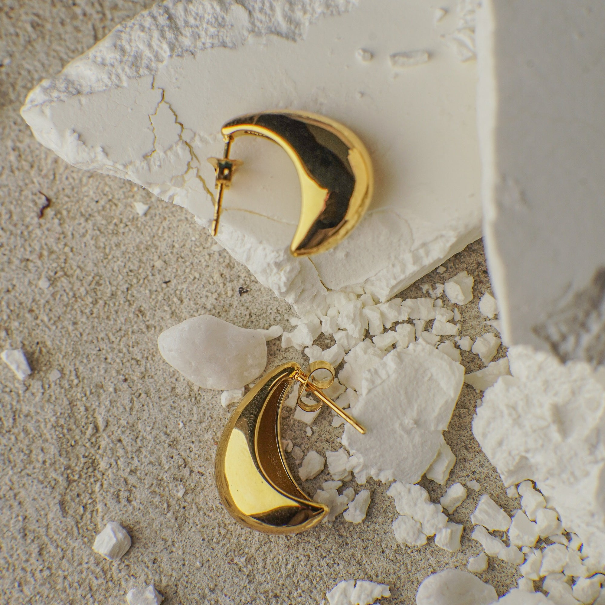 Gold moon-shaped earrings on a textured stone surface