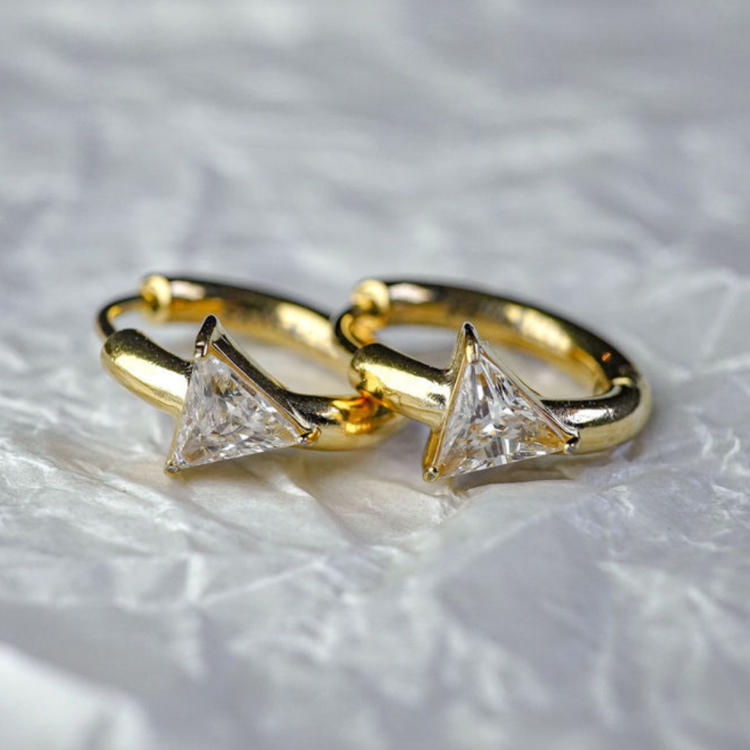 Gold hoop earrings with triangle-shaped gemstones on a textured gray background