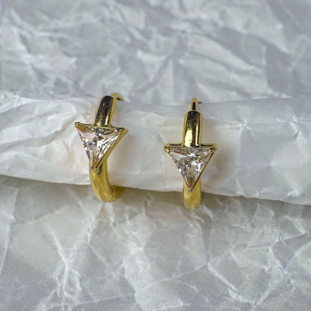 Gold triangle-shaped earrings on a textured white surface