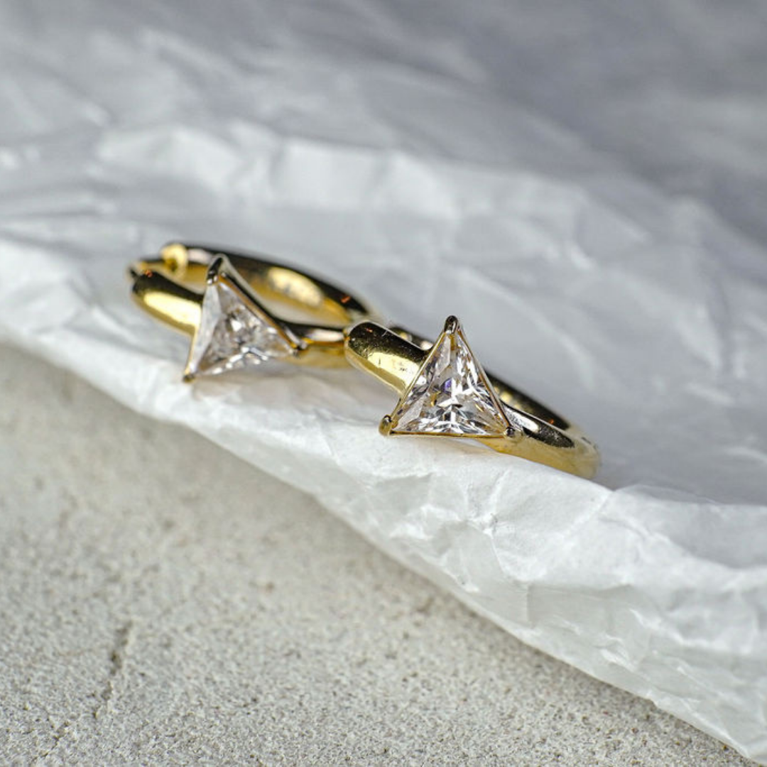 Gold earring with triangle-shaped gemstones on a textured surface
