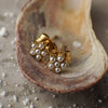 Gold earrings with pearls inside a shell on sand