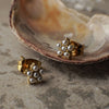 Pair of gold earrings with pearl-like stones on a stone surface.