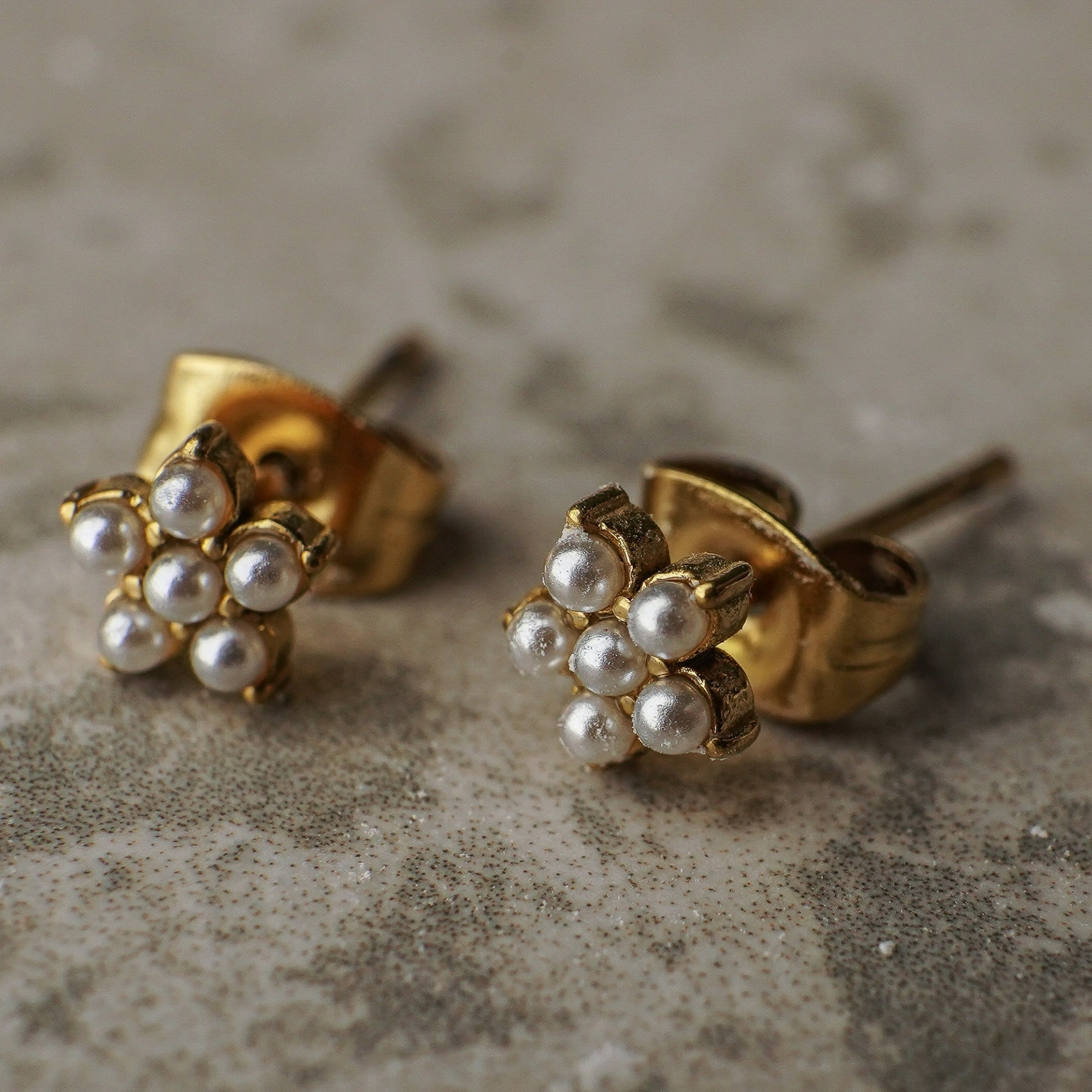 Pair of gold and pearl stud earrings on a textured surface
