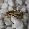 Gold ring with braided design on white pebbles
