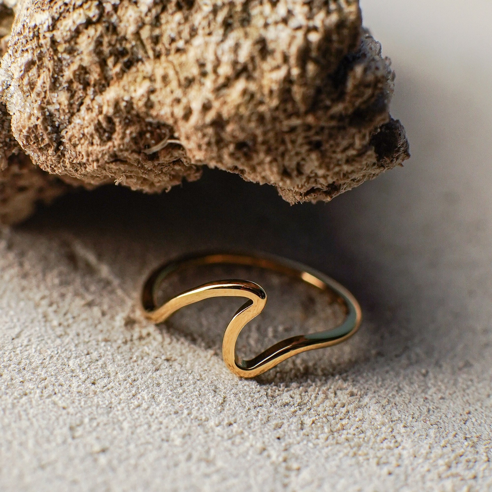 Gold ring on sand with a rock in the background