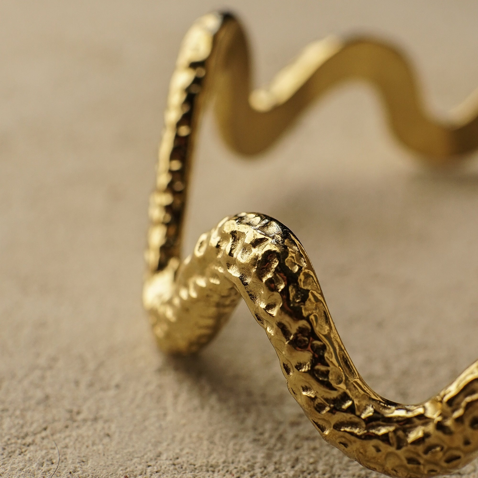 Gold snake-shaped bracelet on a textured beige surface