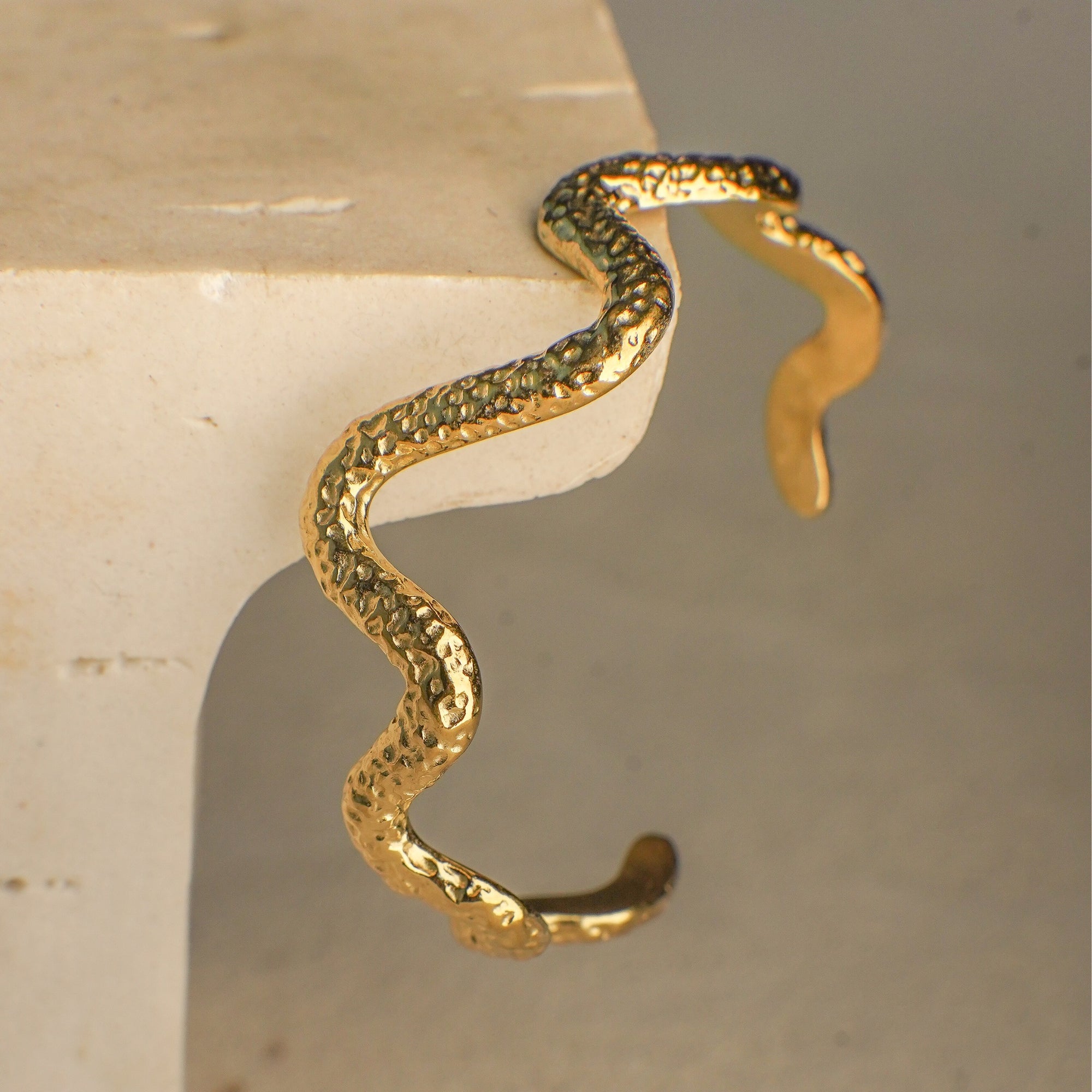Gold snake-shaped bracelet on a beige surface
