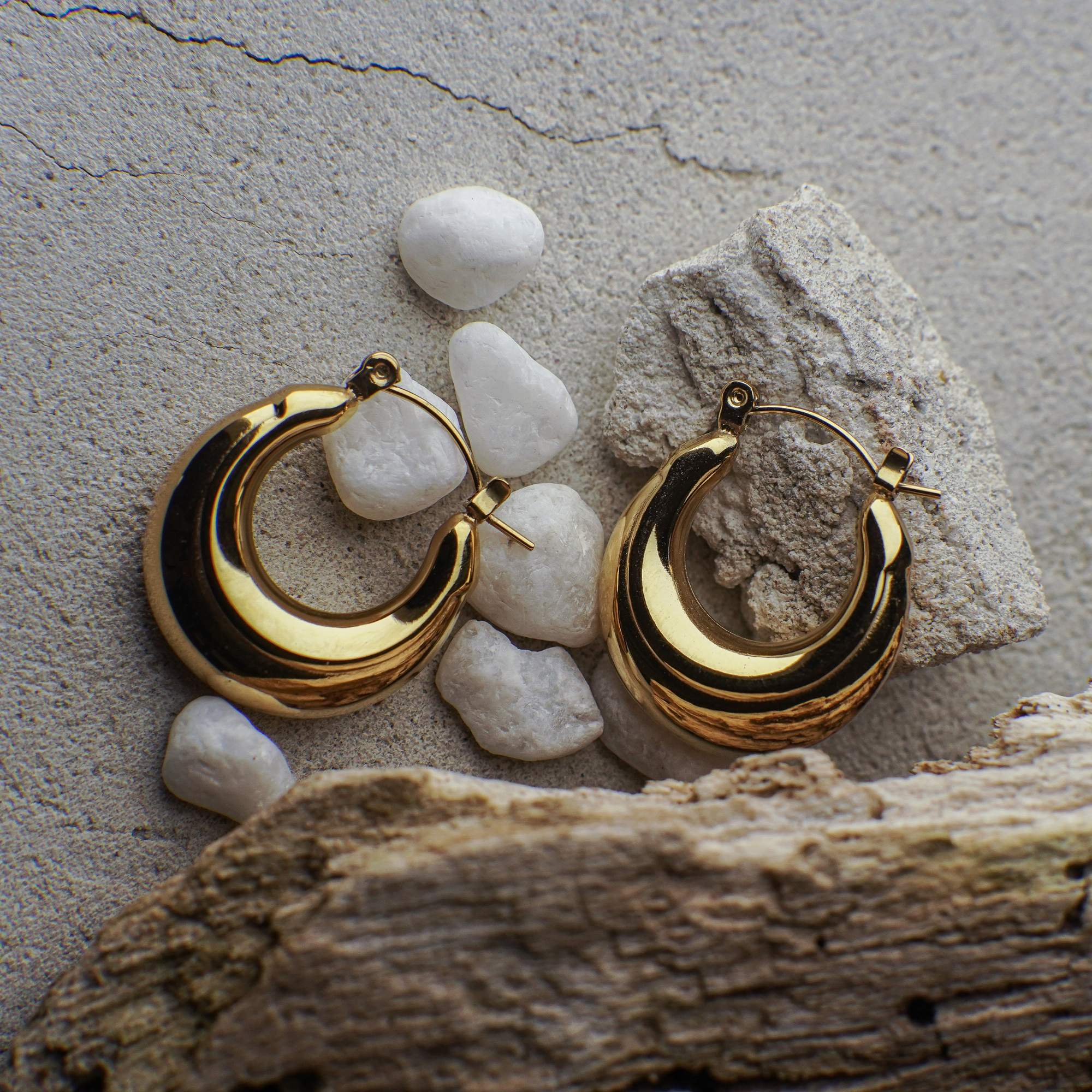 Gold hoop earrings on a textured stone surface with pebbles