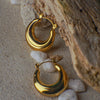 Gold hoop earrings on a textured surface with pebbles