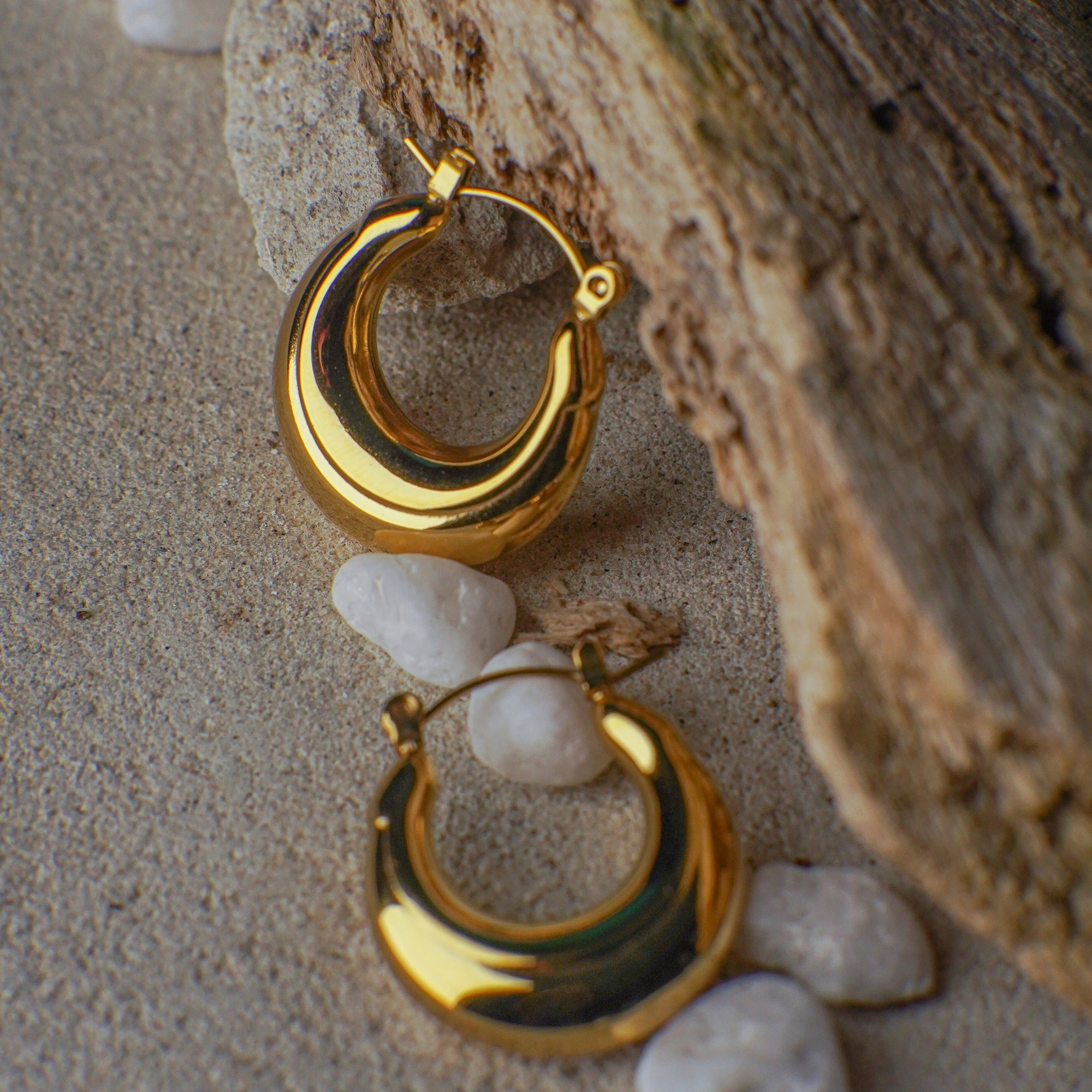 Gold hoop earrings on a textured surface with pebbles
