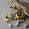 Gold hoop earrings on a stone surface with small stones around