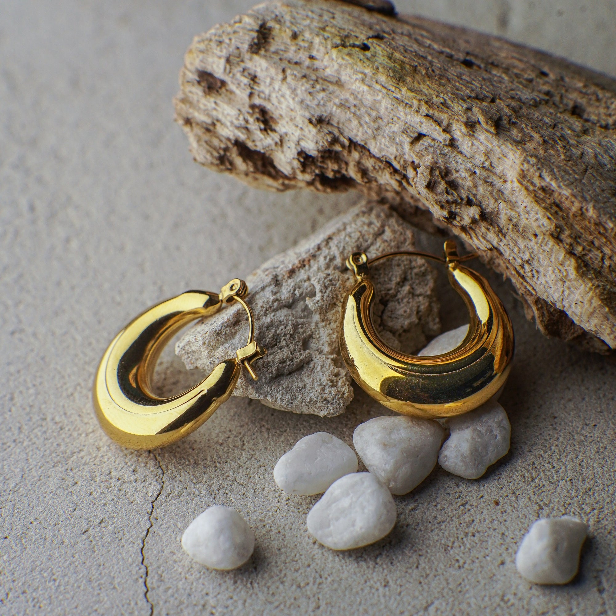 Gold hoop earrings on a stone surface with small stones around