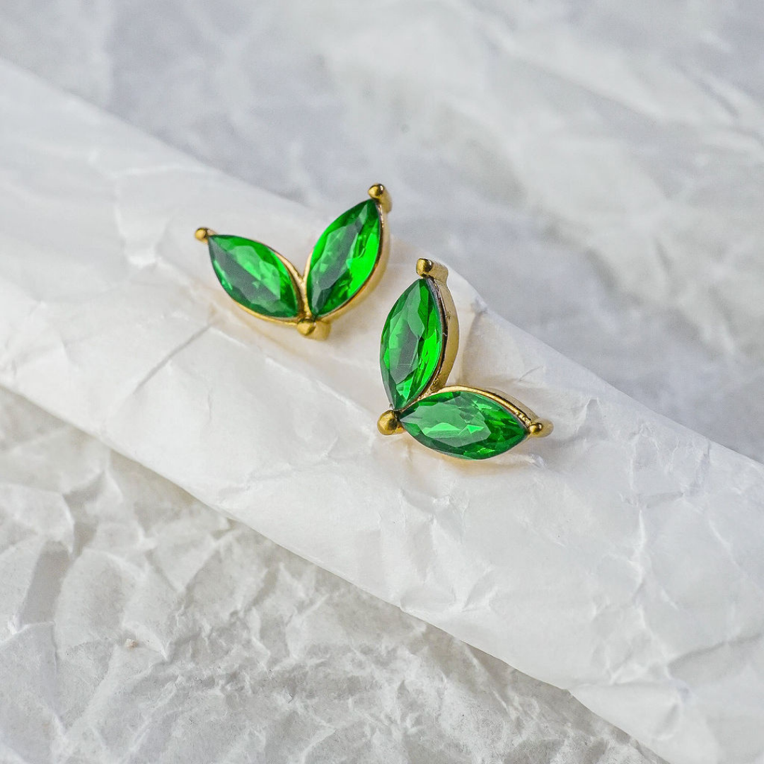 Green gemstone earrings with gold setting on a textured white background