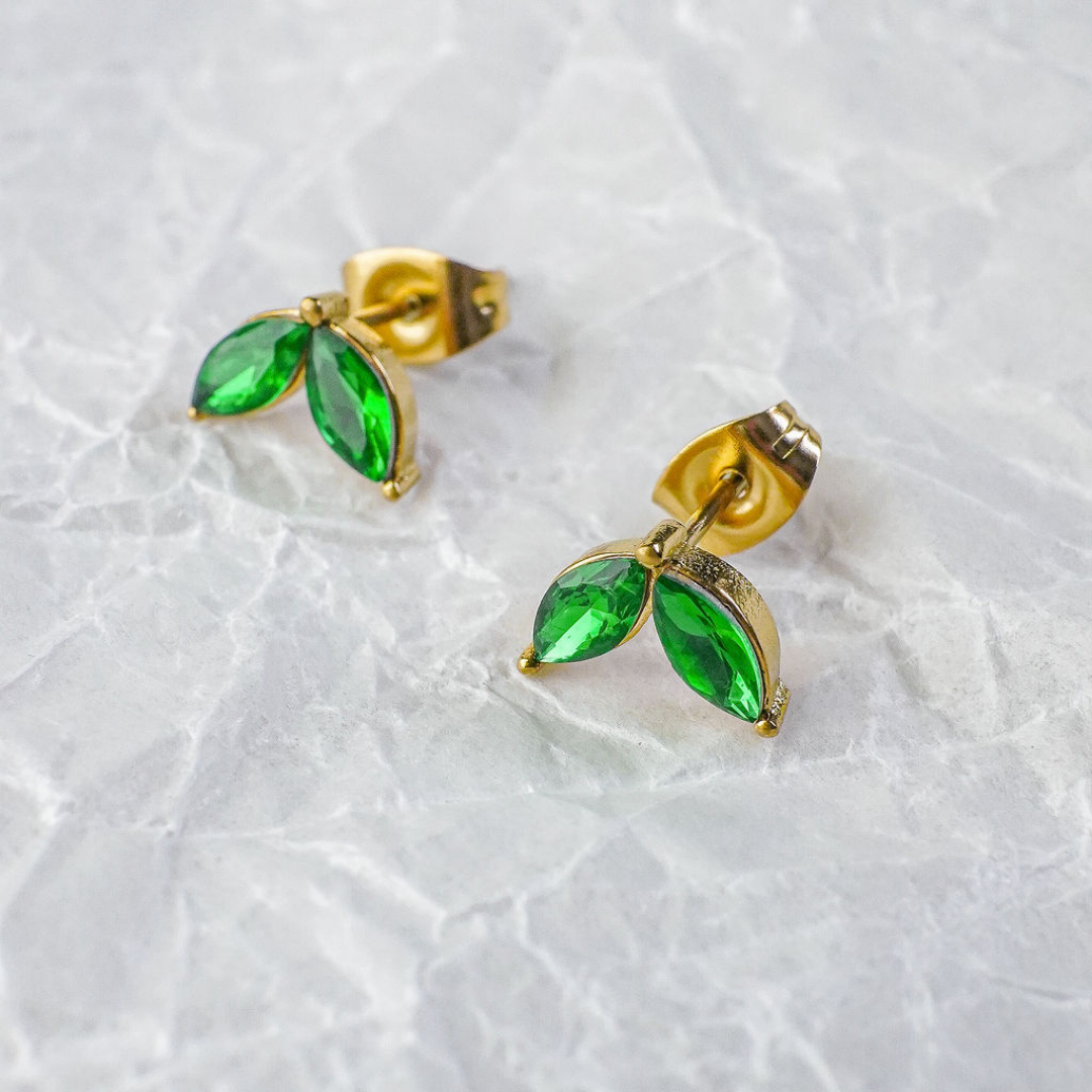 Gold earrings with green gemstones on a textured white background
