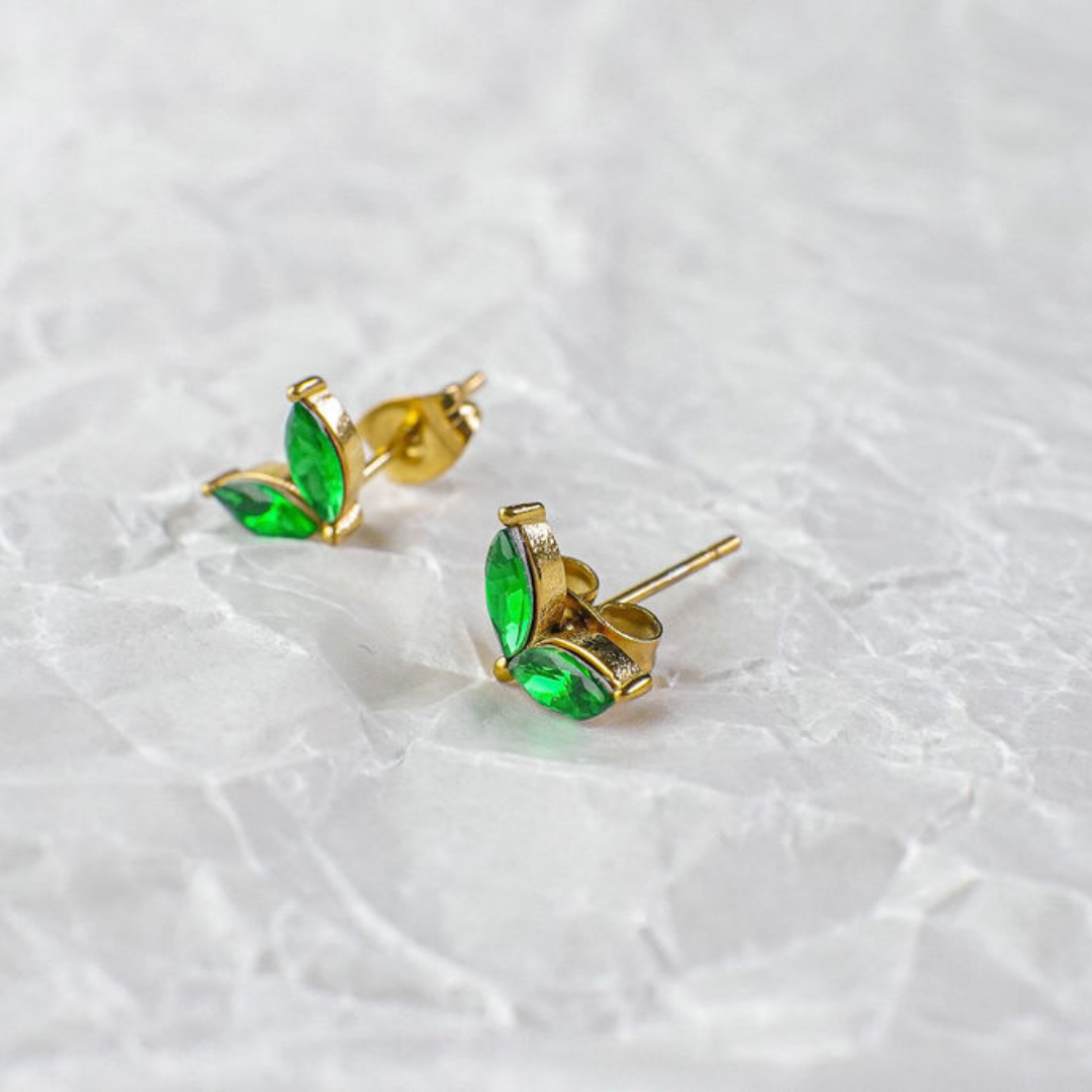 Gold earrings with green gemstones on a light gray background