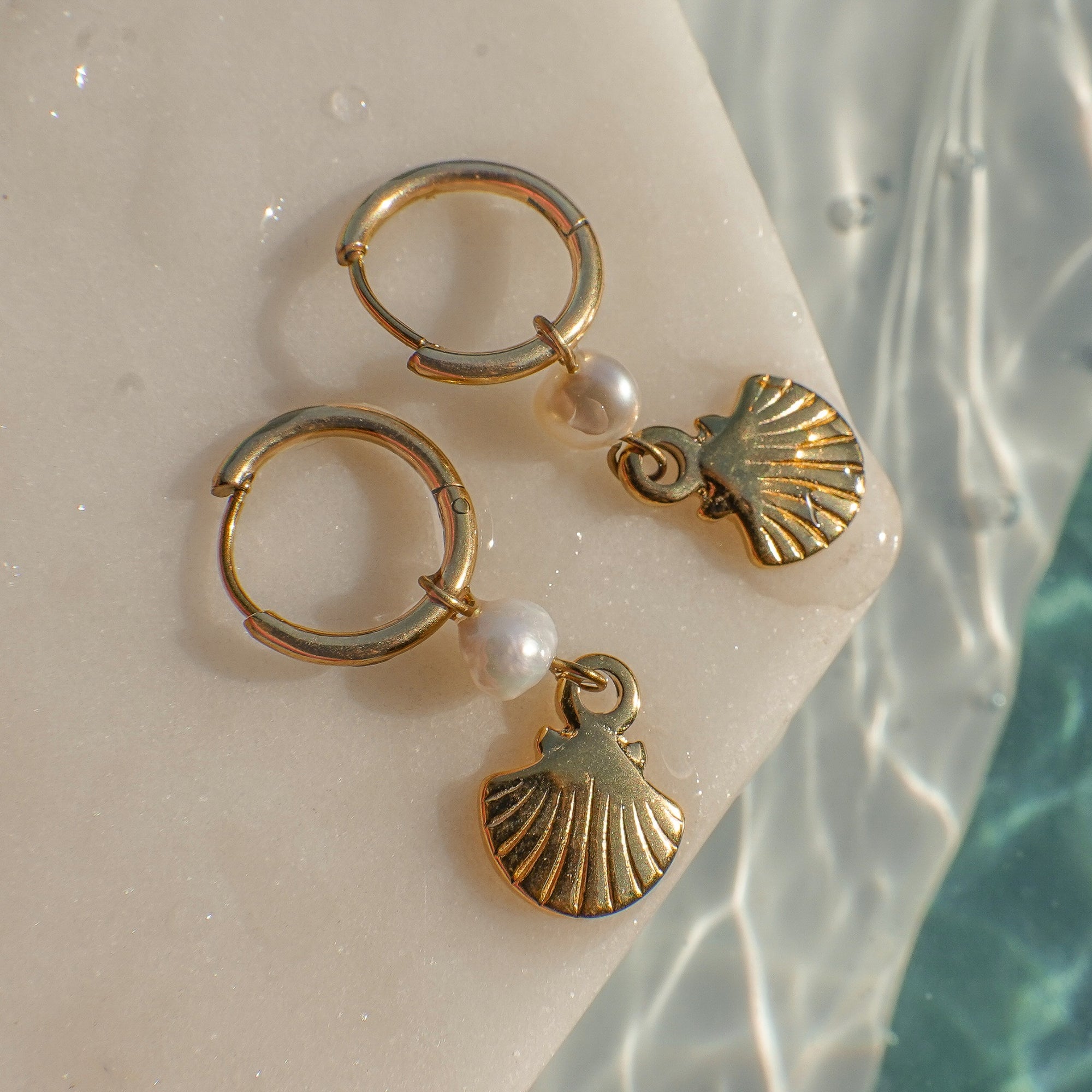 Gold hoop earrings with shell and pearl charms on a light background
