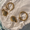 Gold hoop earrings with shell charms on a textured white surface