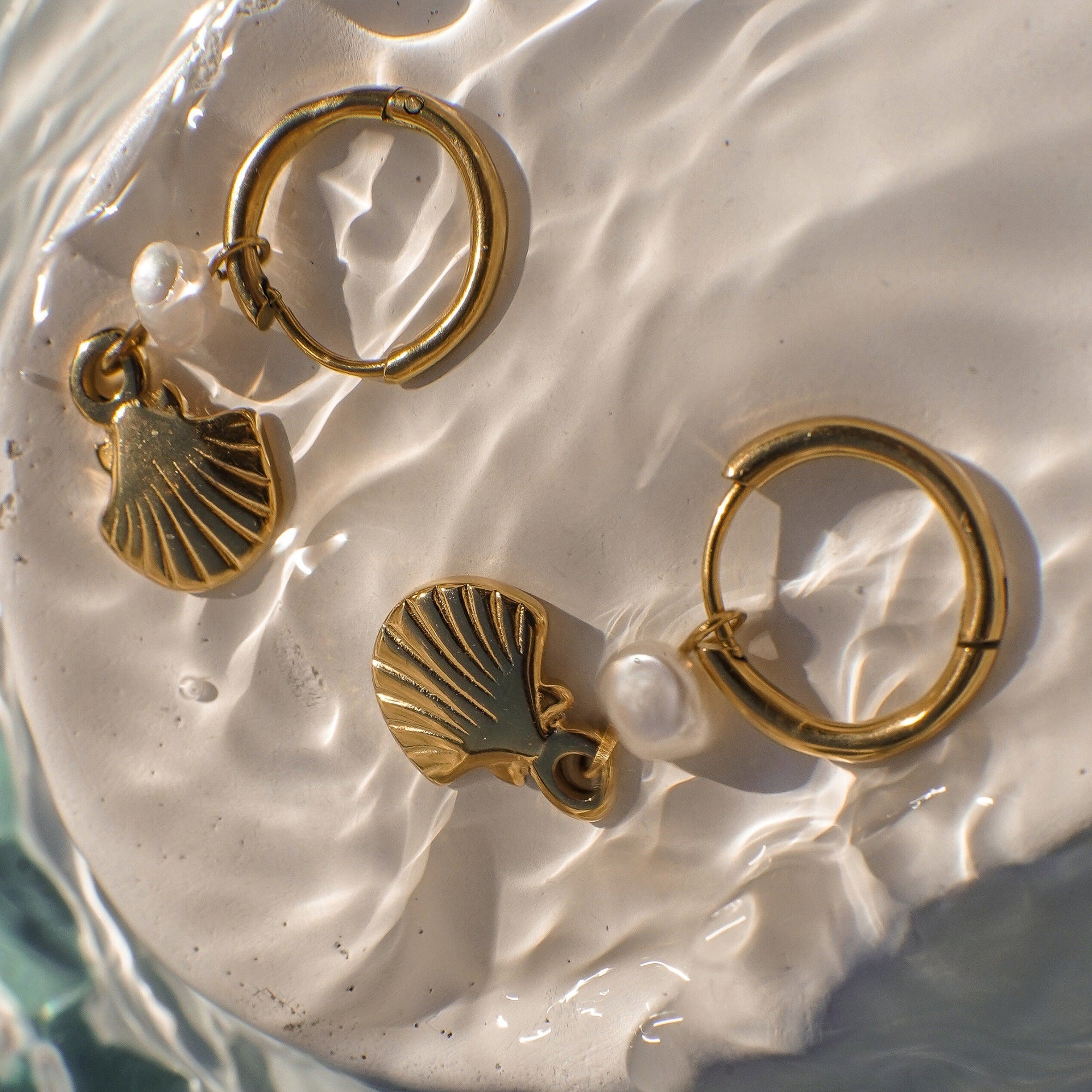 Gold hoop earrings with shell charms on a textured white surface