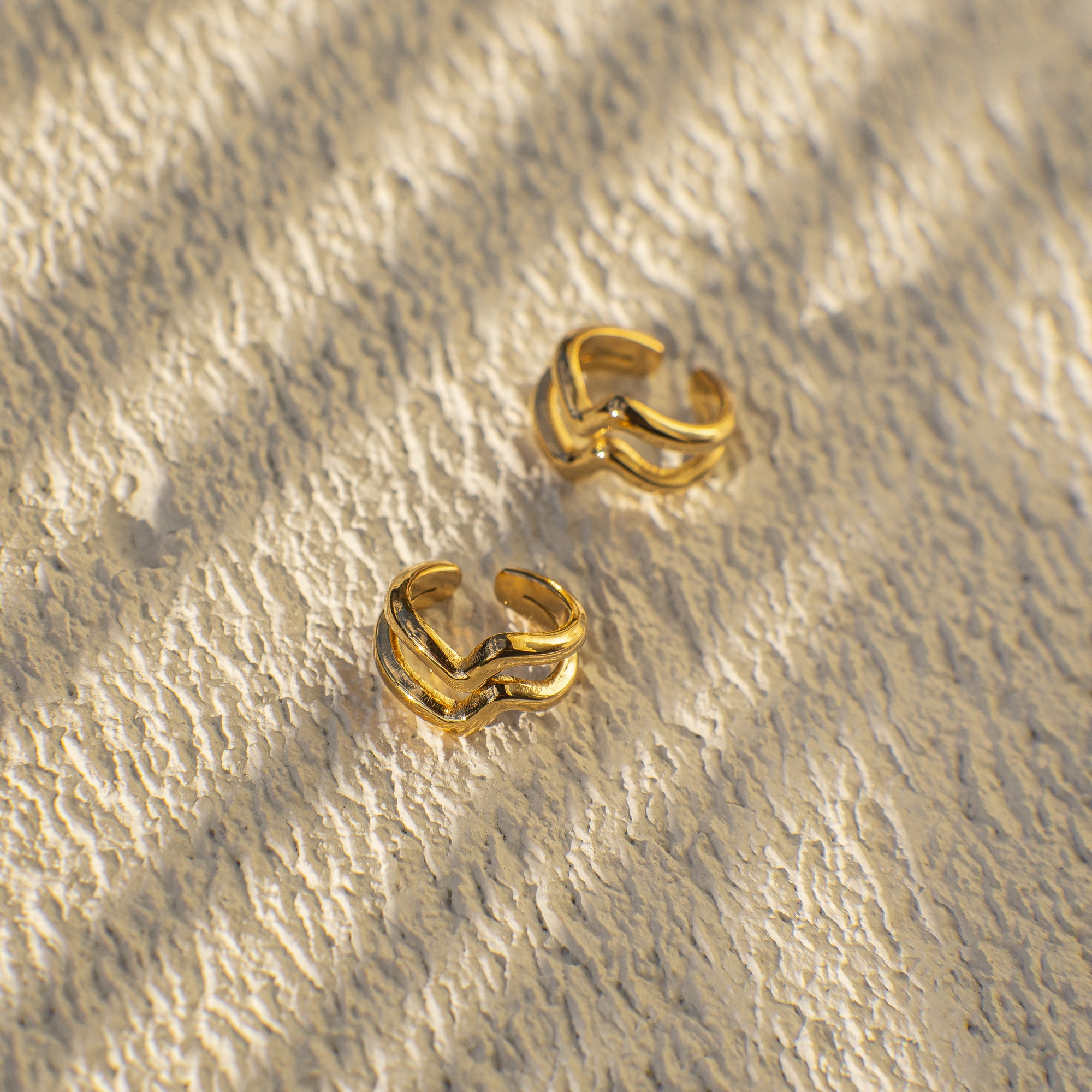 Pair of gold hoop earrings on a textured beige surface